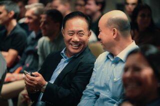 Carousel 1 - Slide 2 Two men smiling and chatting at a conference