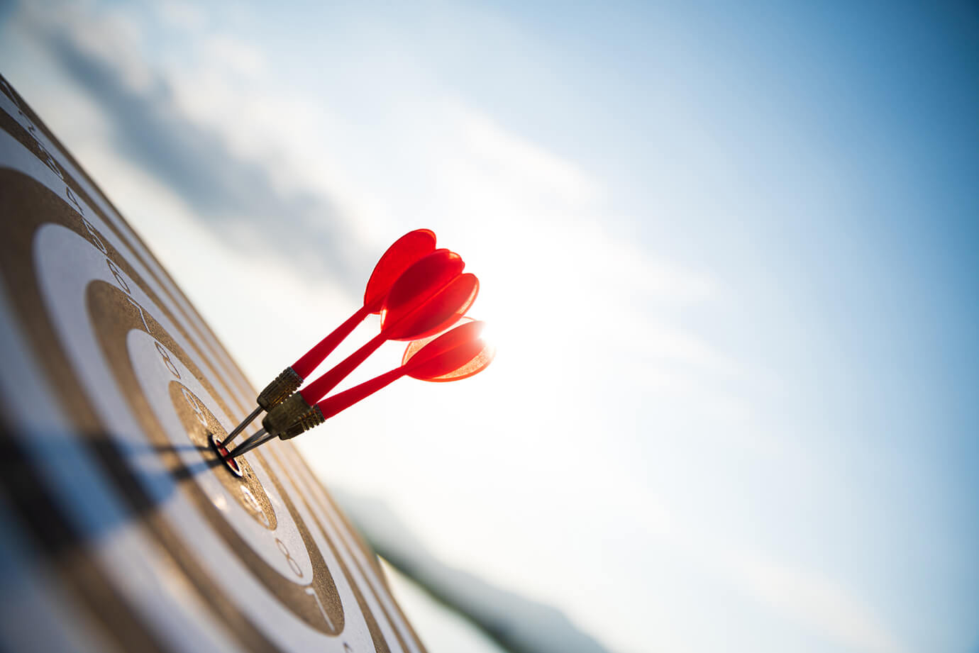M&A: Buy-Side Image Close up shot red darts arrows in the target center on dark blue sky background. Business target or goal success and winner concept