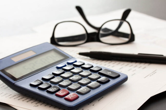 Calculator, glasses, pen and papers on white fading background with copy space