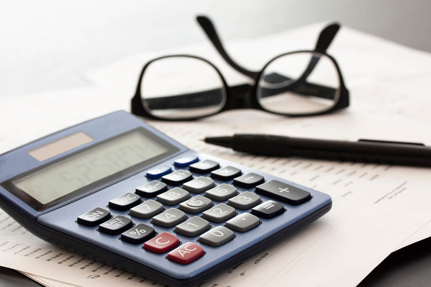 Calculator, glasses, pen and papers on white fading background with copy space