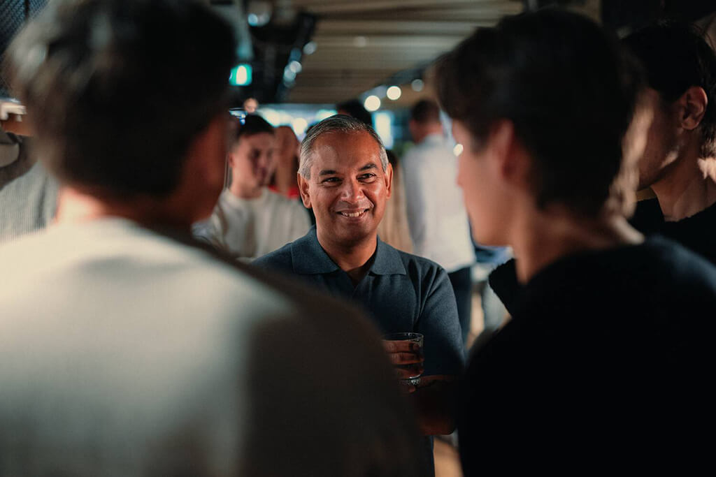 Who We Are Man smiling with a group in conversation